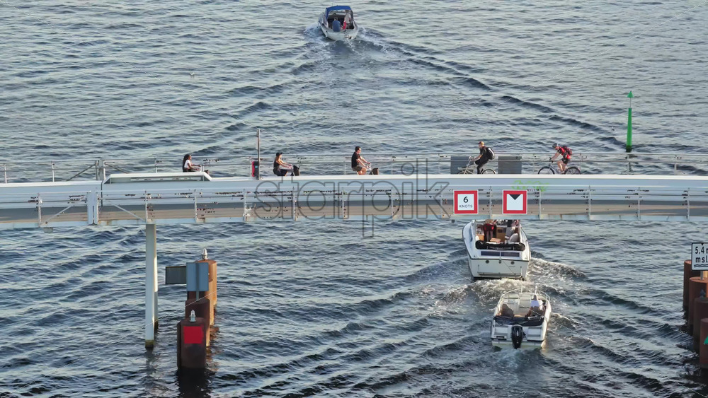 Video - Copenhagen, Denmark - August 6, 2025: Aerial drone view of the Lille Langebro pedestrian bridge with people cycling and walking across the harbour at sunset in Copenhagen, Denmark