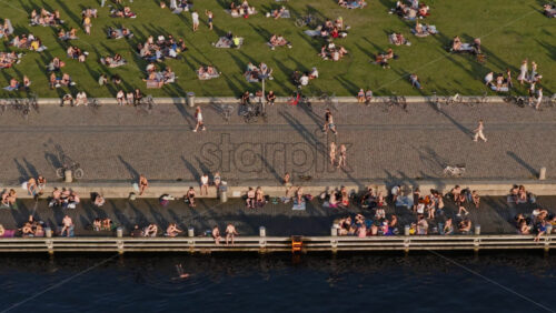 Video - Copenhagen, Denmark - August 6, 2025: Aerial view of locals gathering on the green lawn and along the harbor edge in the evening sun at Havneparken, Islands Brygge