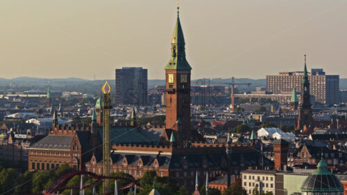 Video - Copenhagen, Denmark - August 6, 2025: Aerial drone view of the Copenhagen City Hall tower, Tivoli rides, and old city rooftops