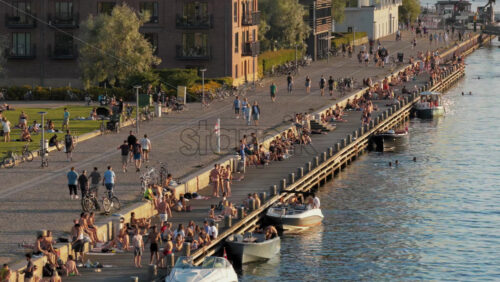 Video - Copenhagen, Denmark - August 6, 2025: Aerial view of locals gathering on the green lawn and along the harbor edge in the evening sun at Havneparken, Islands Brygge