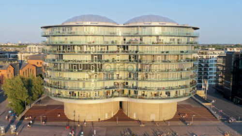 Video - Copenhagen, Denmark - August 6, 2025: Aerial drone view of the Gemini Residence, futuristic round glass building built on old silos, standing at the waterfront of Islands Brygge