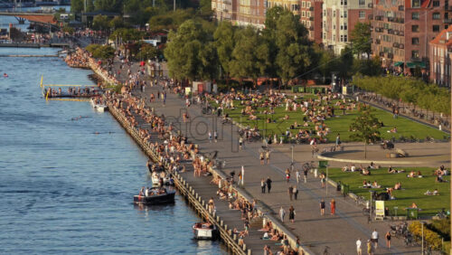 Video - Copenhagen, Denmark - August 6, 2025: Aerial drone view of crowds gathering by the water for swimming, sunbathing, and socialising on a warm evening at Islands Brygge Harbour