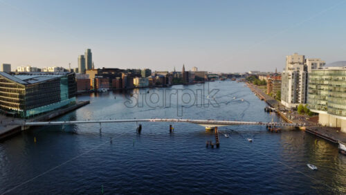 Video - Copenhagen, Denmark - August 6, 2025: Aerial drone view of the Inner Harbour and the Langebro Bridge with boats, cyclists, and the modern city skyline at sunset