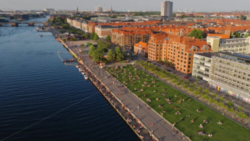 Video - Copenhagen, Denmark - August 6, 2025: Aerial drone view of Islands Brygge park with people relaxing on the grass and the Radisson Blu tower in the background at sunset