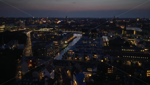 Video - Aerial drone view of Christianshavn with its historic buildings, canals, and the glowing spire of Church of Our Saviour dominating the skyline in the evening in Copenhagen, Denmark