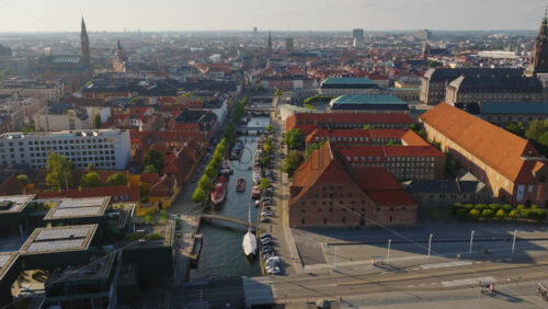 Video - Aerial drone view of Christianshavn canal with red-roofed historic buildings and docked boats in central Copenhagen, Denmark