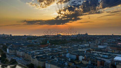 Video - Aerial drone time lapse over Copenhagen rooftops and waterfront with sun rays breaking through the clouds at sunset