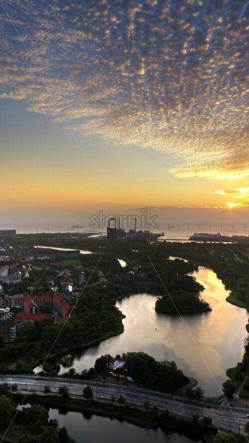 Video - Aerial drone view of Copenhagen, Denmark at sunset with glowing skies, wind turbines in the background. Vertical