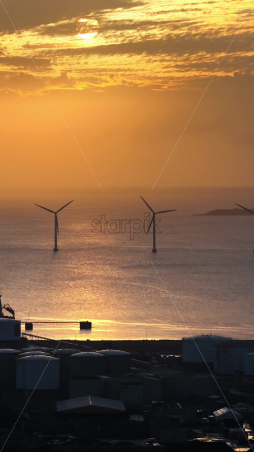 Video - Aerial drone view of the golden sun over the Danish coast, casting light on offshore wind turbines. Vertical