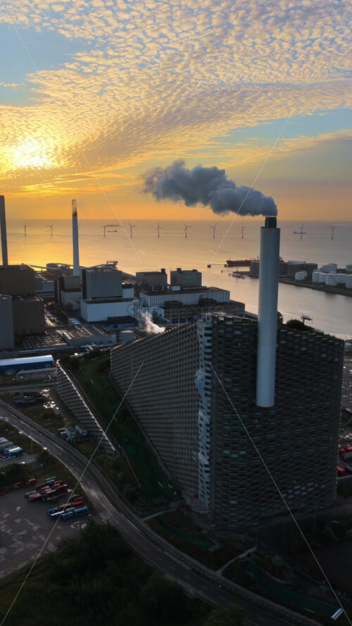 Video - Aerial drone view of CopenHill energy plant with smoking chimneys, overlooking the sea and offshore wind farms in Copenhagen, Denmark. Vertical