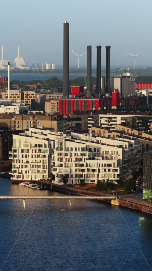 Video - Copenhagen, Denmark - August 3, 2025: Aerial drone view of the Quay Bridge with modern waterfront apartments in Copenhagen, Denmark with canals and wind turbines in the distance. Vertical