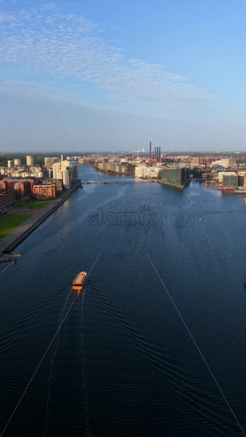 Video - Aerial drone view of the Nyhavn canal and cityscape during golden hour, with boats and modern buildings along the waterfront in Copenhagen, Denmark. Vertical