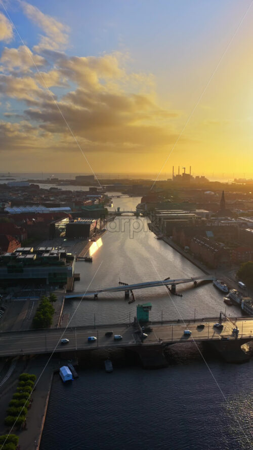 Video - Aerial drone view of Copenhagen's canals and bridges at sunrise, with golden light illuminating the city and harbor. Vertical