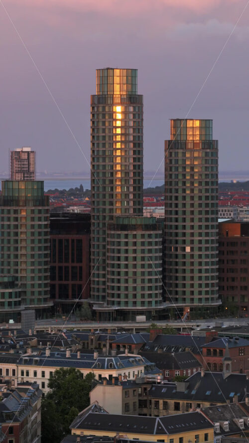 Video - Aerial drone view of modern high-rise towers reflecting the warm glow of the evening sun, standing tall above Copenhagen's skyline. Vertical