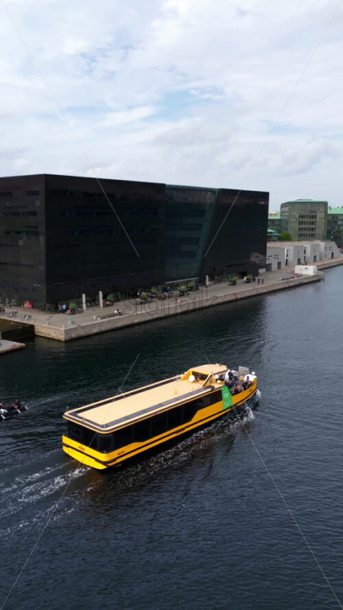 Video - Copenhagen, Denmark - August 4, 2025: Aerial drone view of boat moving near the modern glass extension of the Royal Danish Library. Vertical