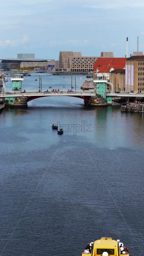 Video - Copenhagen, Denmark - August 4, 2025: Aerial drone view of a yellow harbor bus ferry cruising along the Copenhagen harbor with bridges and city architecture in the background. Vertical