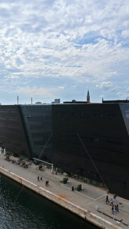 Video - Copenhagen, Denmark - August 4, 2025: Aerial drone view of the modern Black Diamond library by the waterfront, showcasing its striking dark glass design. Vertical