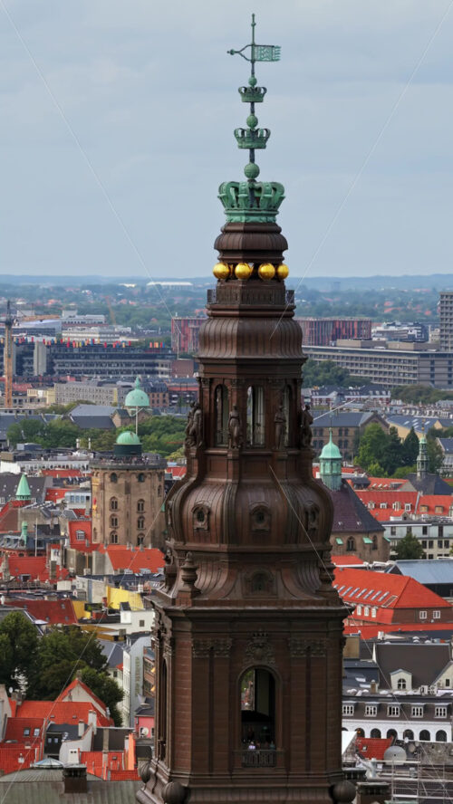 Video - Aerial drone view of the ornate spire of Christiansborg Palace, crowned with golden spheres and intricate details, overlooking the cityscape of Copenhagen, Denmark. Vertical