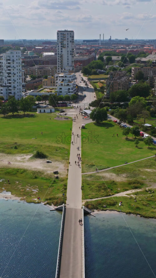 Video - Aerial drone view of a long pedestrian bridge crossing the water, connecting the green park area to the city in Copenhagen, Denmark. Vertical