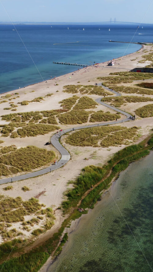 Video - Aerial drone view of Amager Strandpark beach and promenade, with people sunbathing and walking along the pier. Vertical