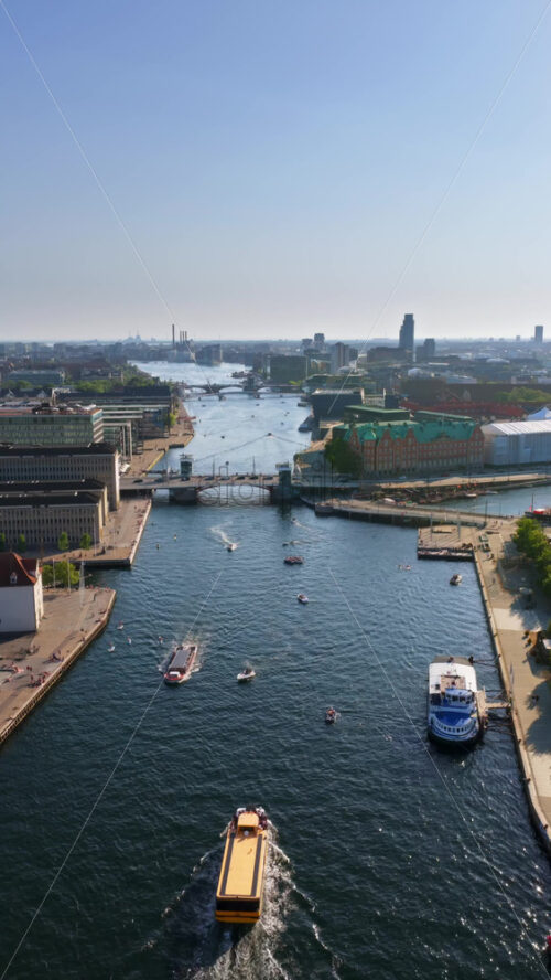 Video - Aerial drone view of Copenhagen's harbor, featuring canals, bridges, and boats, with the yellow harbor bus cruising through the water. Vertical