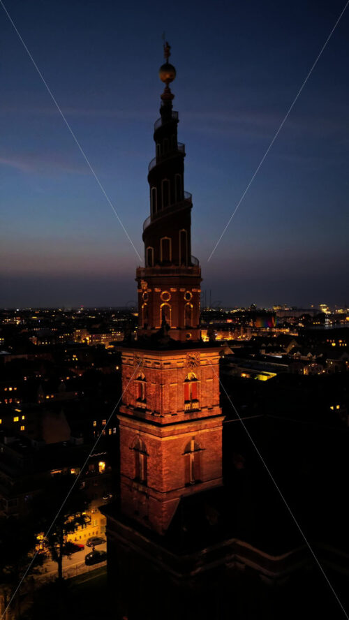 Video - Aerial drone view of the skyline with the famous spiral spire of the Church of Our Saviour lit against the evening sky in Copenhagen, Denmark. Vertical