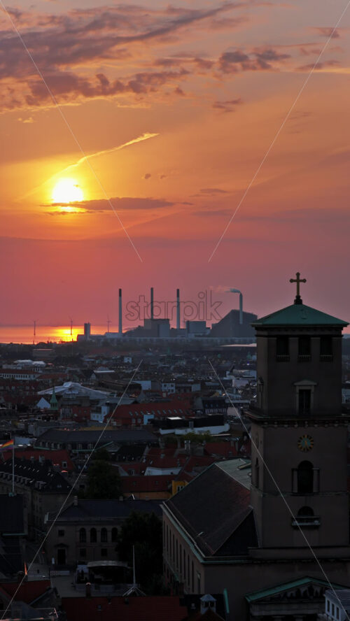 Video - Aerial drone view of the Church of Our Lady, its tower crowned with a cross, surrounded by the city's rooftops and skyline at sunset in Copenhagen, Denmark. Vertical