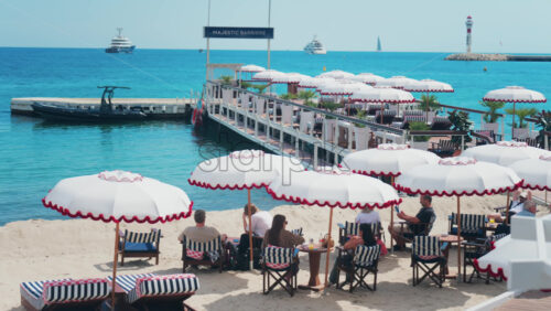 Video - Cannes, France - May 13, 2025: People relaxing under sun umbrellas at a terrace on the beach