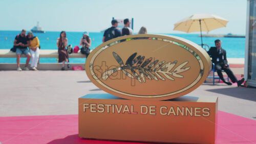 Video - Cannes, France - May 13, 2025: The Cannes Film Festival golden sign on a red carpet with people walking in the background