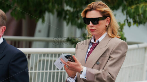 Video - Cannes, France - May 13, 2025: Woman wearing sunglasses and a suit checking her phone on the street