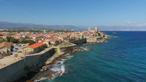 Video - Aerial drone view of Antibes Old Town and its coastal fortifications, with waves crashing against the walls and the Picasso Museum rising above the Mediterranean