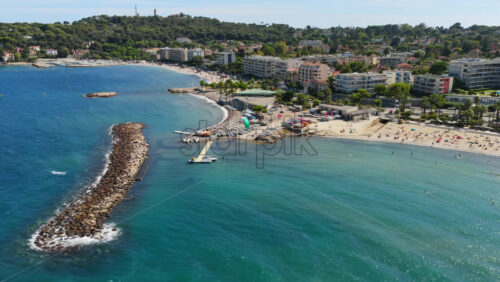 Video - Aerial drone view of Antibes sandy beach with sunbathers, stone breakwaters, and sailing boats docked near the shoreline