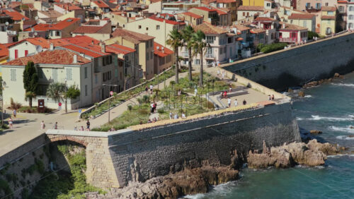 Video - Aerial drone view of Antibes Old Town with terracotta rooftops, palm trees, and medieval fortifications overlooking the Mediterranean Sea