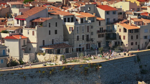 Video - Aerial drone view of Antibes Old Town houses with terracotta rooftops and seaside promenade, with visitors enjoying the historic coastal atmosphere