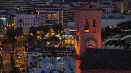 Video - Cannes, France - September 3, 2025: Aerial drone view of the historic clock tower at dusk, with the bustling city center and the Casino Barriere in the background, glowing with evening lights