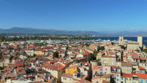 Video - Aerial drone view of Antibes Old Town with medieval ramparts, terracotta rooftops, marina, and surrounding mountains in the distance