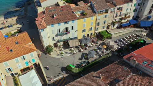 Video - Aerial drone view of Antibes Old Town square with outdoor cafes, parasols, and historic Mediterranean buildings near the ramparts