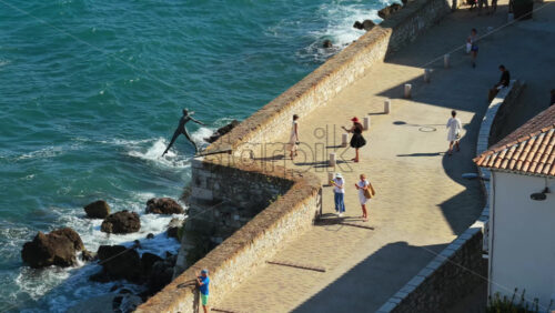 Video - Antibes, France - September 4, 2025: Aerial drone view of the bronze sculpture Le Nomade along the ramparts with waves crashing on the rocks below