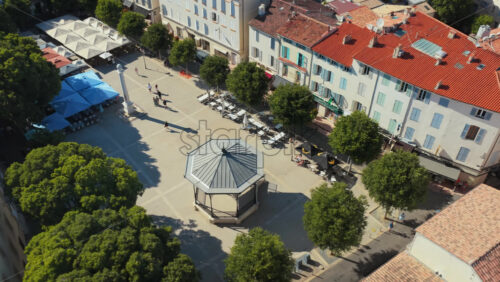 Video - Aerial drone view of Place Nationale in Antibes, with trees, outdoor cafes, monument, and bandstand in the historic town center