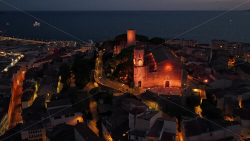 Video - Aerial drone view of Cannes Old Port and the medieval Suquet quarter, with yachts docked in the marina and the Church of Our Lady of Esperance beautifully illuminated
