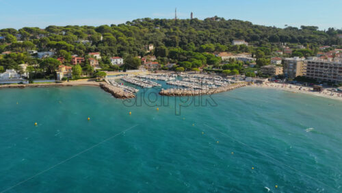 Video - Aerial drone view of Antibes small port and marina with sailboats docked, sandy beaches, and green hills in the background