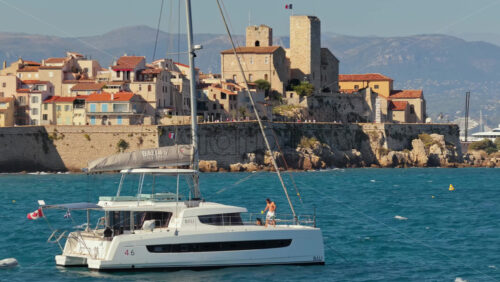 Video - Antibes, France - September 4, 2025: Aerial drone view of a luxury catamaran sailing in front of Antibes Old Town and its medieval stone ramparts