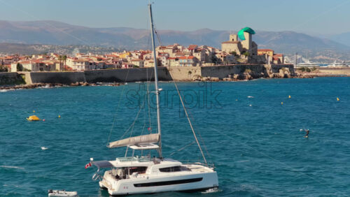 Video - Antibes, France - September 4, 2025: Aerial drone view of a luxury catamaran sailing in front of Antibes Old Town and its medieval stone ramparts