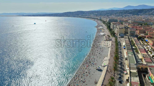Video - Aerial drone view of the Bay of Angels in Nice, with the Promenade des Anglais, turquoise Mediterranean waters, and parasailers in the distance