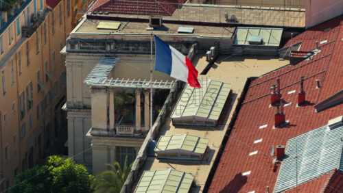 Video - Aerial drone view of a French flag waving above a historic building in central Nice, with rooftops in the background