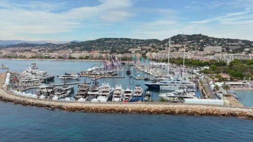 Video - Aerial drone view of Cannes harbor filled with luxury yachts, sailboats, and seafront hotels in the background