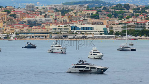Video - Aerial drone view of luxury yachts anchored offshore with the Palais des Festivals and Cannes city skyline in the background