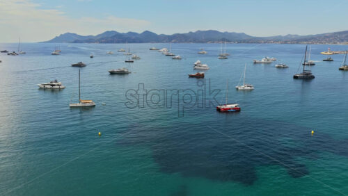 Video - Aerial drone view of dozens of yachts and sailboats anchored in the calm turquoise waters off Cannes