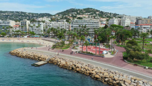 Video - Aerial drone view of the promenade, beachfront park with palm trees, and nearby residential buildings, Cannes, France