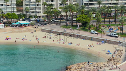 Video - Cannes, France - September 6, 2025: Aerial drone view of the sandy beach with umbrellas, sunbathers, and swimmers in turquoise sea